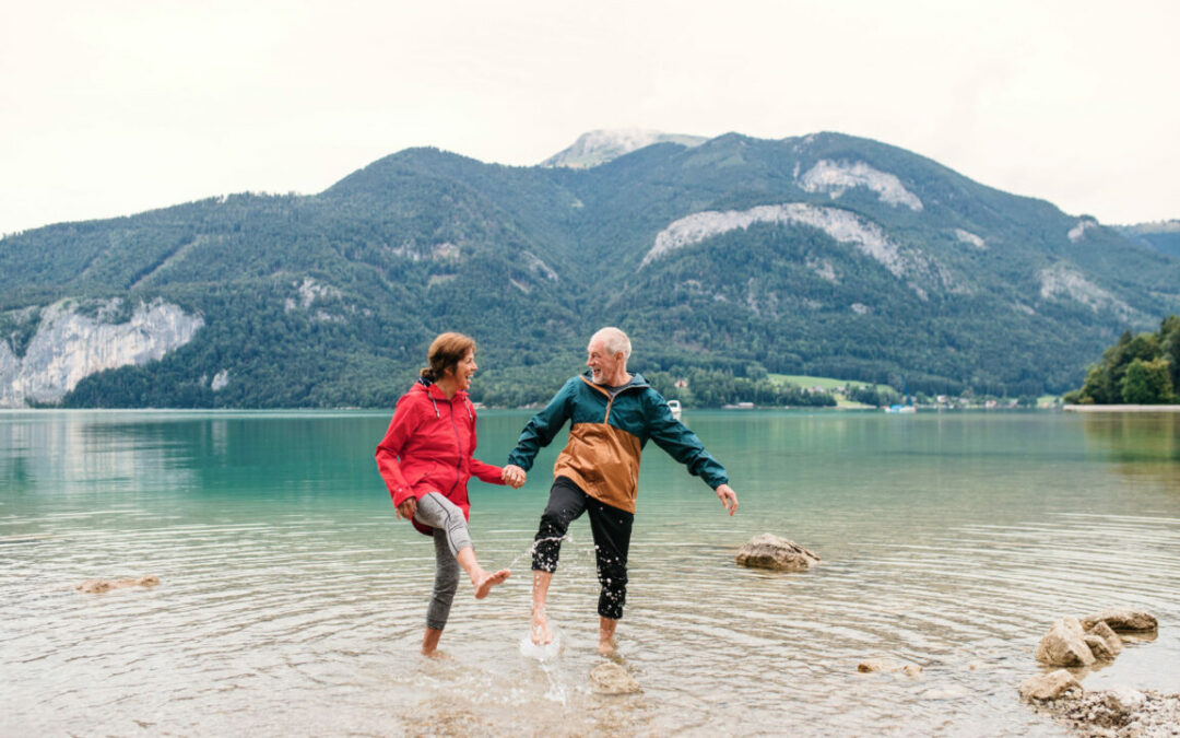 Older couple holding hands in water with mountains in background